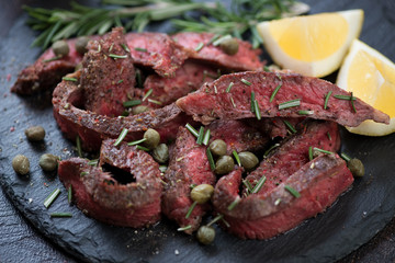Close-up of tagliata beefsteak with olive oil, capers, chopped fresh rosemary and lemon, selective focus, shallow depth of field