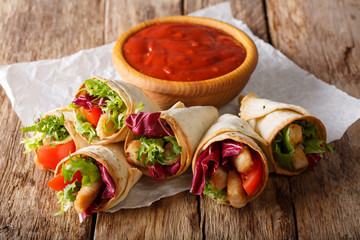 Burrito rolls with turkey, lettuce and tomato close-up on paper and ketchup on the table. horizontal