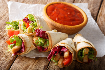Homemade burrito with turkey, lettuce and tomato close-up on paper and ketchup. horizontal