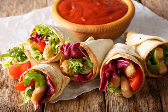 Freshly cooked burritos with turkey, lettuce and vegetables close up on a paper on the table. horizontal