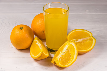 Glass of orange juice and fresh oranges on white wooden table