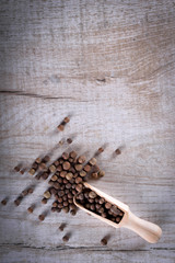 Pepper peas in a wooden spoon on a wooden background. Spices are scattered on the table
