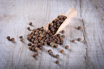 Pepper peas in a wooden spoon on a wooden background. Spices are scattered on the table