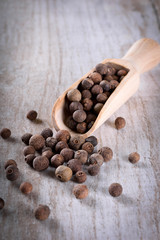 Pepper peas in a wooden spoon on a wooden background. Spices are scattered on the table