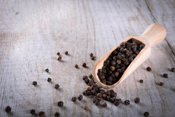 Pepper peas in a wooden spoon on a wooden background. Spices are scattered on the table