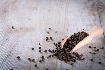 Pepper peas in a wooden spoon on a wooden background. Spices are scattered on the table