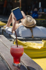 Watermelon smoothie on the beach table. Women are resting  with tablet in her hand. Lipe island,Thailand.