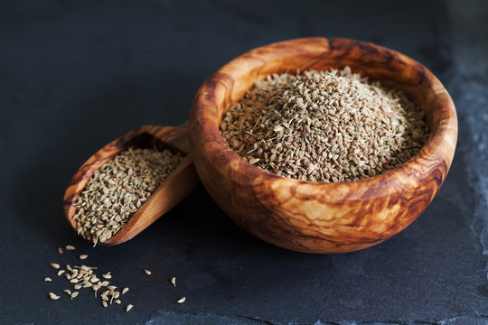 Closeup of ajwain seeds in a wooden bowl over darl slate background