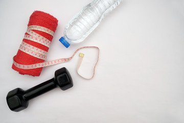 Fitness concept with dumbbells, measure tape, bottle of mineral water and a red towel on an isolated white background.