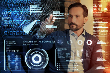 Important analysis. Clever experienced enthusiastic programmer looking at the futuristic transparent screen of his modern device and analyzing different sources of information at the same time