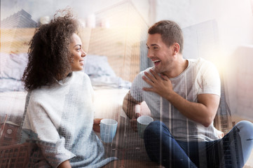 Wonderful time. Nice delighted handsome man holding a cup of tea and laughing while talking to his girlfriend