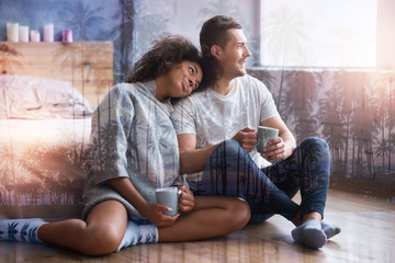 International couple. Nice attractive young woman sitting near her boyfriend and putting her head on his shoulder while holing a cup of tea