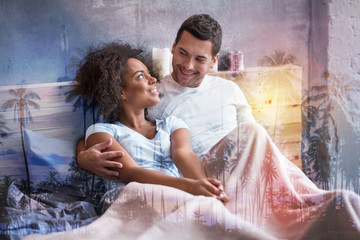 Pleasant morning. Joyful positive delighted couple smiling and looking at each other while lying in bed together