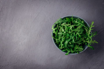Fresh green arugula in bowl on grey stone background. Arugula is rich in vitamins and trace elements. Selective focus. Top view image. Copyspace for your text. Fashion magazine filter.