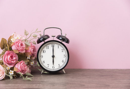 alarm clock and rose on wood table with pink background and copy space for product display montage.