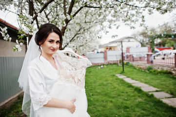 A portrait of a pretty bride posing next to her dress outdoors next to the blossoming tree.