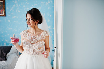 Portrait of a gorgeous bride in her room with perfumes in her hand.