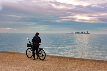 Obraz premium Senior man with his bicycle standing and enjoy the view along the seafront in the sunrise. Thessaloniki, Greece