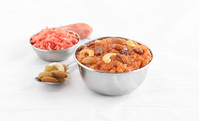 Carrot halwa or pudding, a traditional, popular and delicious Indian sweet dish, along with carrot gratings and almonds, raisins and cashew nuts, in a steel bowl.
