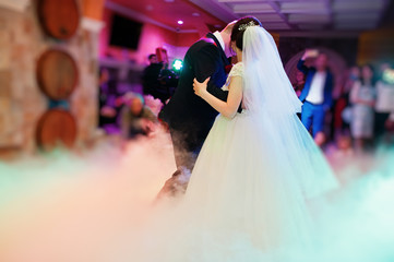 Fototapeta premium Happy young wedding couple dancing their first dance with different lights and heavy smoke in the restaurant on their wedding party.