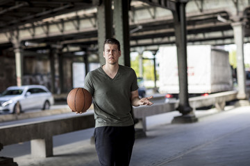 Man With a Basketball Standing Under a City Bridge