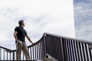 Man Standing on an Outdoor Stairwell and Looking at a Skyscraper