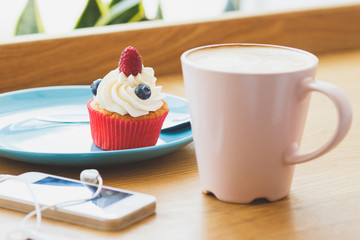 Small cupcake with raspberry and blueberry and a cup of hot cappuccino