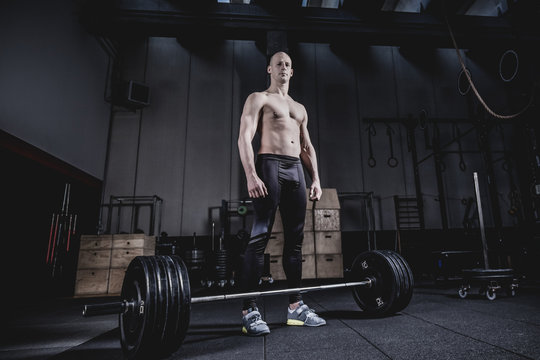 Muscular man Standing at Barbells Before Exercise. Dramatic Color Grading.