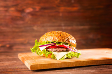 Burger on a wooden board on wooden table over dark background