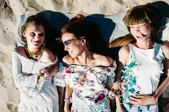 Beautiful Happy Stylish Sexy Young Girls Lying On Sand Beach On Blanket. Show Smile,  Tongue. Party In Style Boho. Maiden Evening Hen-parties. Bachelorette. Close Up Portrait Appearance Above Top View