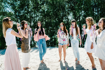 Obraz premium Beautiful happy stylish sexy young girls on sand beach. Drinking champagne. Glasses decorated with ribbons flowers. Party in Style boho. Maiden evening Hen-parties. Bachelorette. Close up