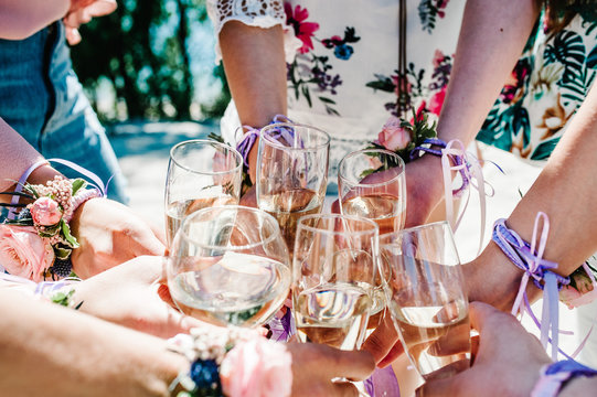 The hands of girls with boutonnieres and ribbons hold and raise glasses of champagne up. champagne glass decorated with flowers. Party in Style boho. Maiden evening Hen-parties. Bachelorette. Close up