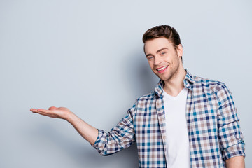 Fototapeta premium Close up portrait of successful, cheerful, cute, professional, young man presenting new product, start up, showing copy space on his palm, standing over grey background