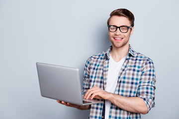 Portrait of bearded, cheerful, brunet guy holding open laptop, looking at camera, searching information through wifi internet, standing over grey background