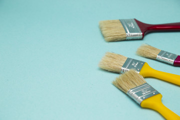 Painting the house. Two red and two yellow paint brushes on blue background with copy space, top view, flat lay