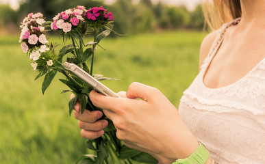 Fototapeta premium Young woman with bouquet of flowers and phone in the nature