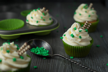 Four cupcakes in green paper with white cream sprinkled with green stars on a dark wooden table