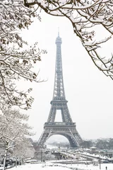 Rolgordijnen The Eiffel tower seen through snow-covered branches on a snowy day in Paris, France, with the top of the tower disappearing slightly in the mist. © olrat