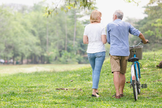 Leisure lifestyle,Senior couple walking their bike along happily talking in the park, rear view of an older caucasian walk in a park