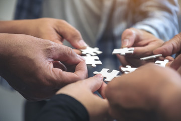 Closeup image of many people hands holding a jigsaw puzzle in circle together