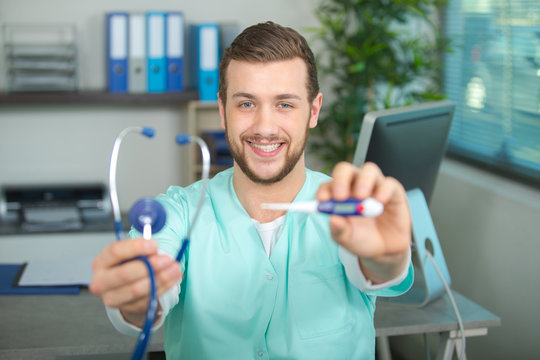 male pediatrician smiling and holding thermometer and stethoscope