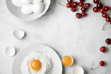 Ingredients for clafouti with cherries and egg on a white background.