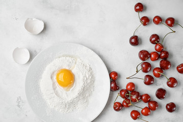 Ingredients for clafouti with cherries and egg on a white background.