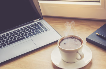 Close up view on work desk interior with laptop computer and morning coffee cup. Toned photo of work desk with computer and coffee cup.