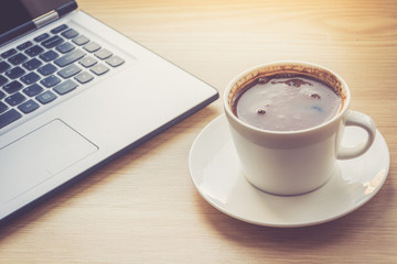 Close up view on work desk interior with laptop computer and morning coffee cup. Toned photo of work desk with computer and coffee cup.