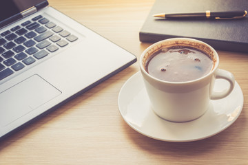Close up view on work desk interior with laptop computer and morning coffee cup. Toned photo of work desk with computer and coffee cup.