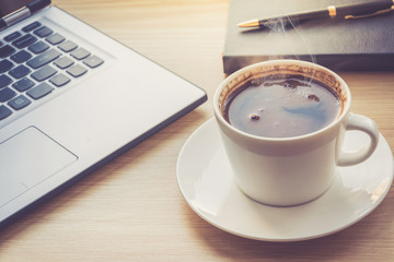 Close up view on work desk interior with laptop computer and morning coffee cup. Toned photo of work desk with computer and coffee cup.