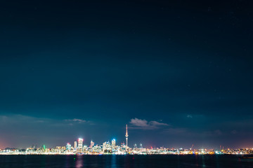 Fototapeta premium Clear starry sky above Auckland city’s skyline with the harbour, the ocean and some boats at the front