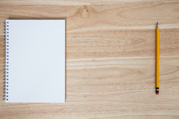yellow pencil with note book on wood table
