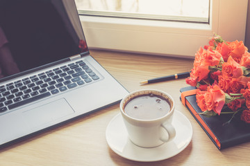 Work desk interior with a laptop computer and morning coffee cup. Toned photo of female work desk with computer and coffee cup.